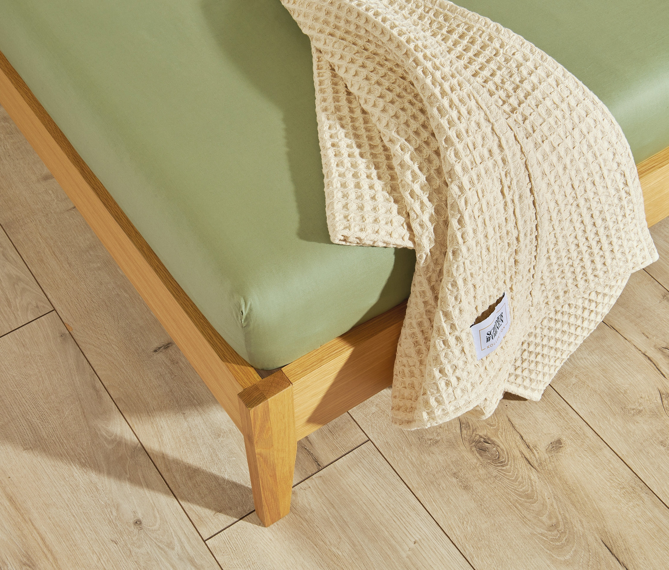Grünes SCHÖNER WOHNEN Perkal-Spannbettlaken auf einem Holzbettrahmen mit einer beige Decke an der Seite.