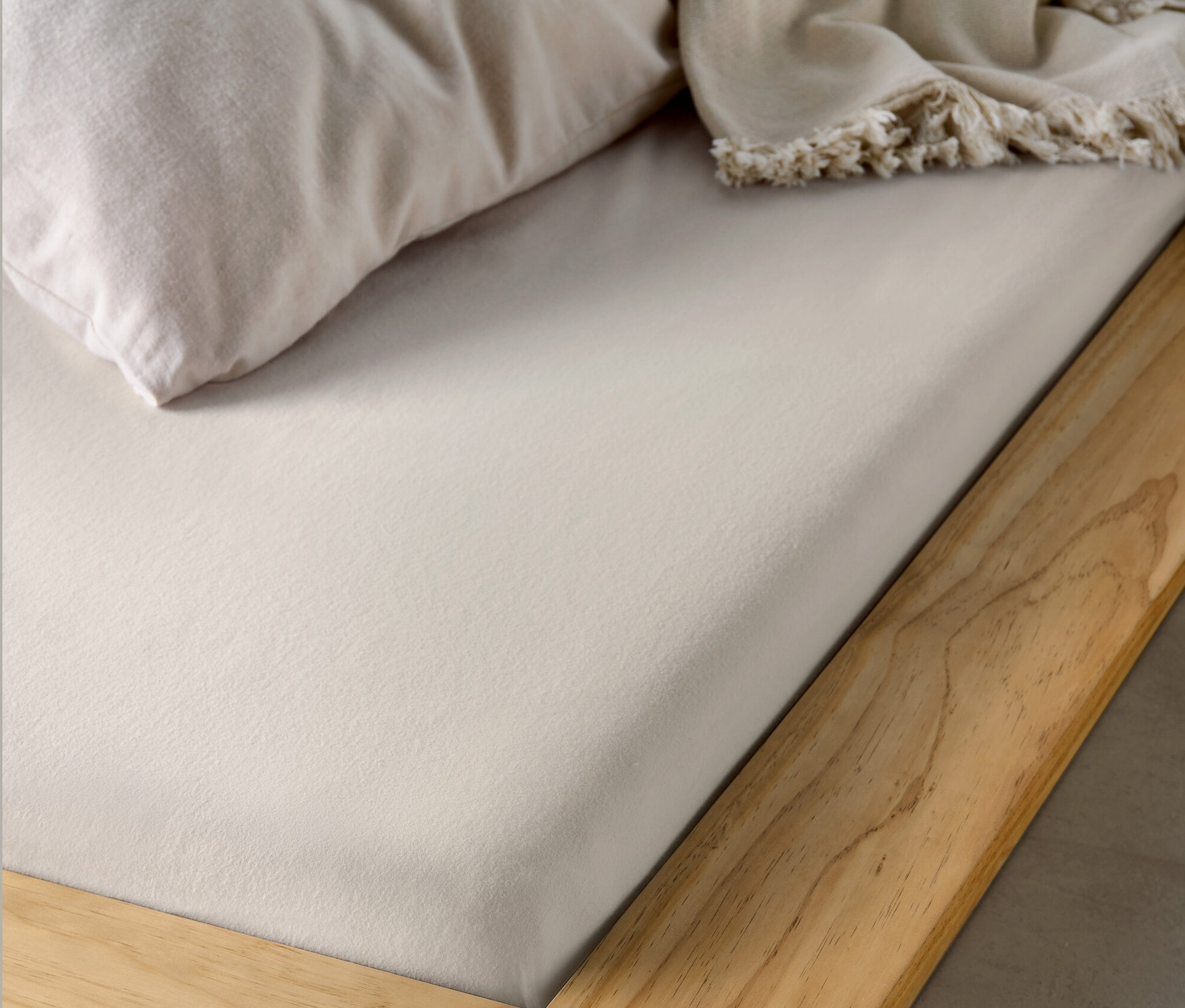 Detailansicht eines Holzbettgestells mit einem beige Biber-Spannbettlaken.