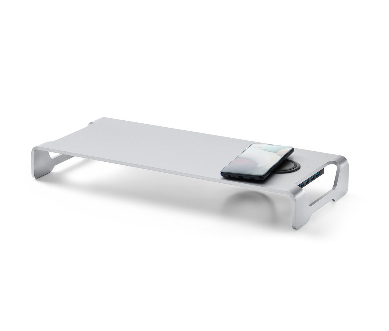 Ein silberner Monitorständer mit kabelloser Ladestation und USB-Hub. Auf der Ladestation liegt ein Handy.