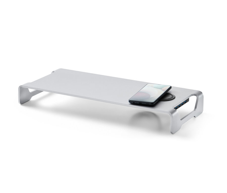 Ein silberner Monitorständer mit kabelloser Ladestation und USB-Hub. Auf der Ladestation liegt ein Handy.