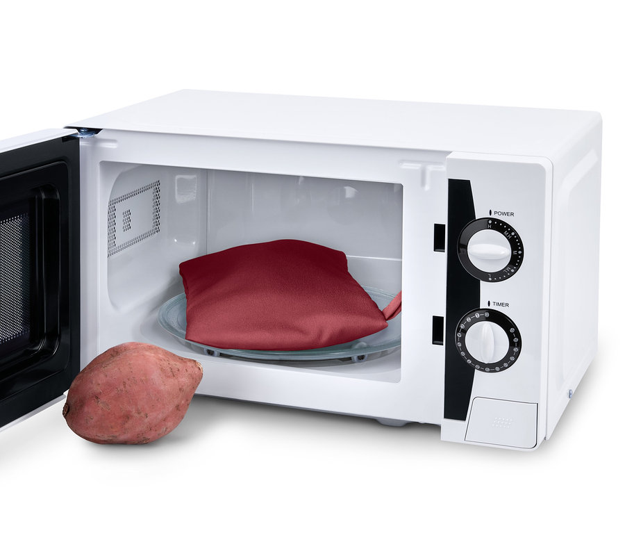 Eine rote Mikrowellen-Kartoffel-Gartasche liegt auf einem Glasteller im Mikrowellenherd, daneben liegt eine Kartoffel.