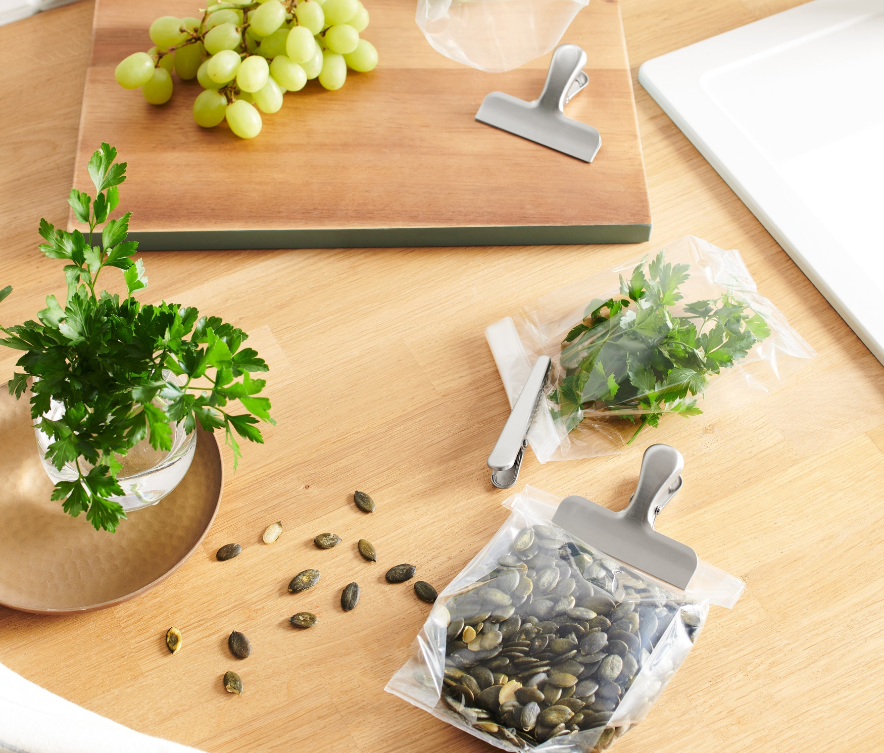 Auf einem Holztisch liegen Trauben, Petersilie im Glas, Kürbiskerne und 3 Edelstahl Aroma-Clips an den Beuteln.