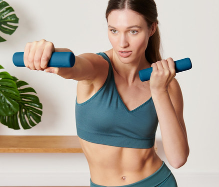 Frau macht Übungen mit 2 Hanteln.