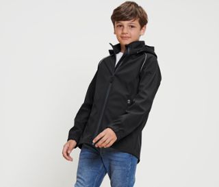 Ein Junge posiert in einer schwarzen Kinder-Softshelljacke.