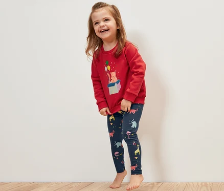 Lächelndes Mädchen trägt einen roten Pullover und 5 Kinder-Leggings mit Tiermotiven.