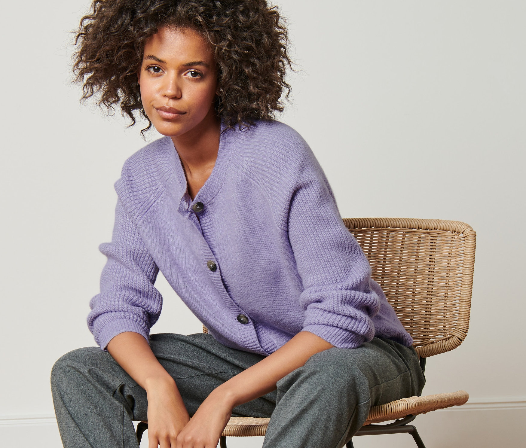 Frau sitzt auf einem Stuhl und trägt einen Strickcardigan.
