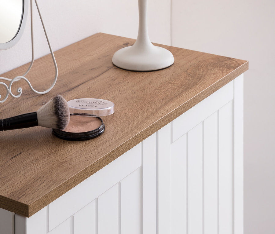 Detailaufnahme eines Highboards »Jelda« in Mattweiß mit Eiche-Dekor, darauf liegen ein Pinsel, ein Puder, eine Lampe und ein Spiegel.