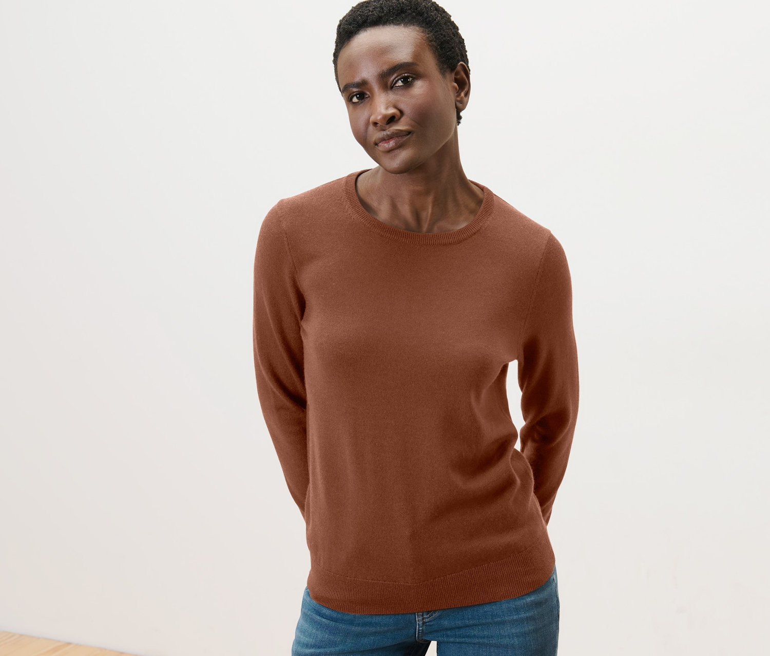 Frau posiert in einem Merino-Feinstrickpullover in Cognac-Farbe und Jeans.