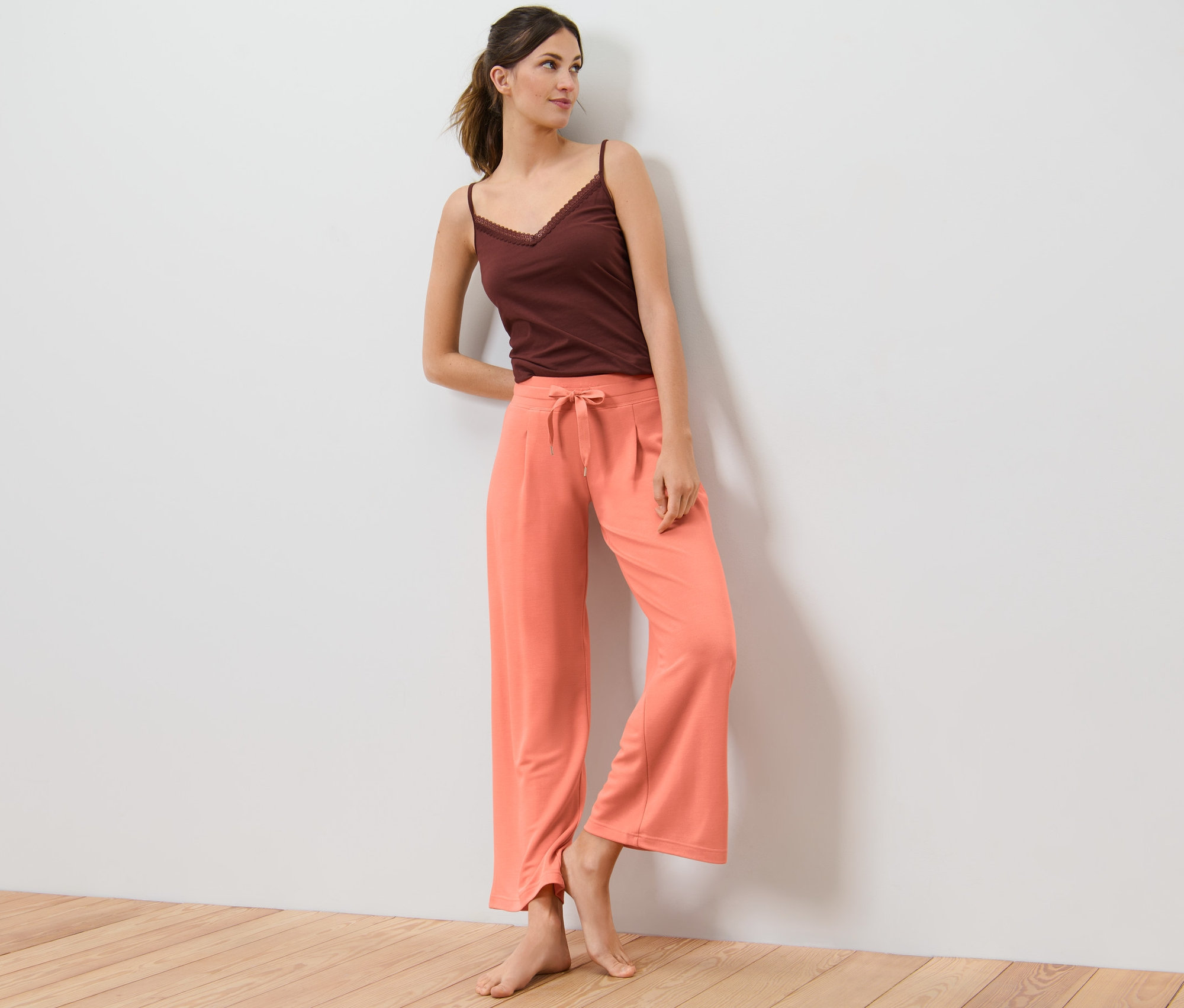 Frau lehnt an Wand, trägt Loungewear-Hose und braunes Top.