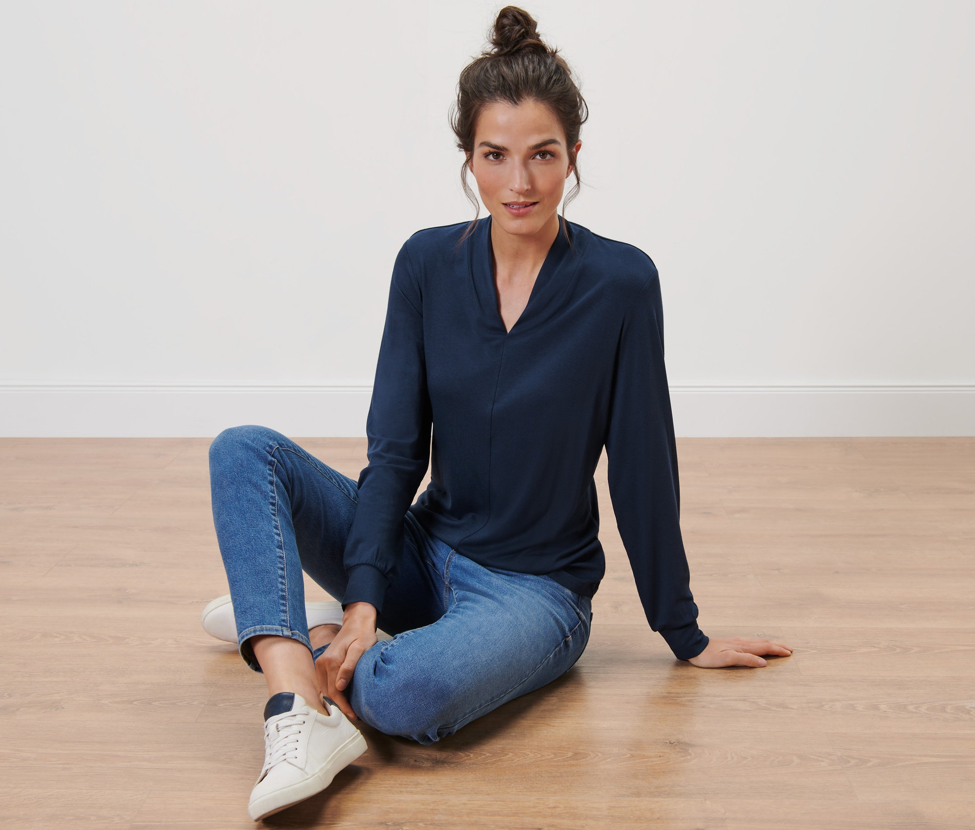 Frau sitzt auf dem Boden und trägt ein dunkelblaues Langarmshirt mit V-Ausschnitt.