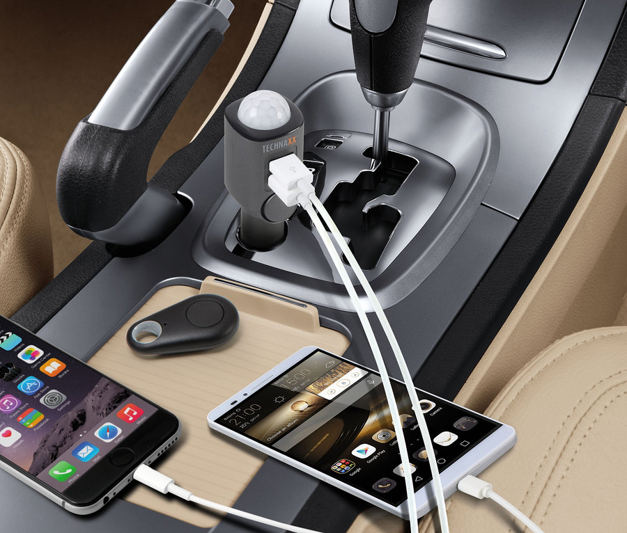 Zwei Mobiltelefone werden im Auto geladen. Daneben befindet sich ein kleiner, schwarzer Alarm. TECHNAXX Mobiler Mini-Alarm mit Bewegungsmelder ist auch sichtbar.