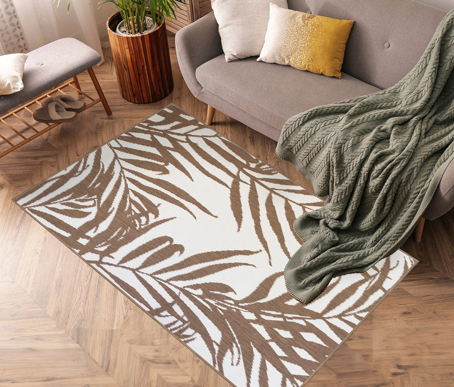 Ein brauner Outdoor-Wendeteppich »Palm Tree« liegt in einem Wohnzimmer mit grauem Sofa und grüner Decke.