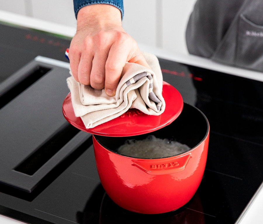 Eine Hand hält ein Tuch auf einem roten STAUB Kochtopf »La Cocotte« mit 16 cm Durchmesser.