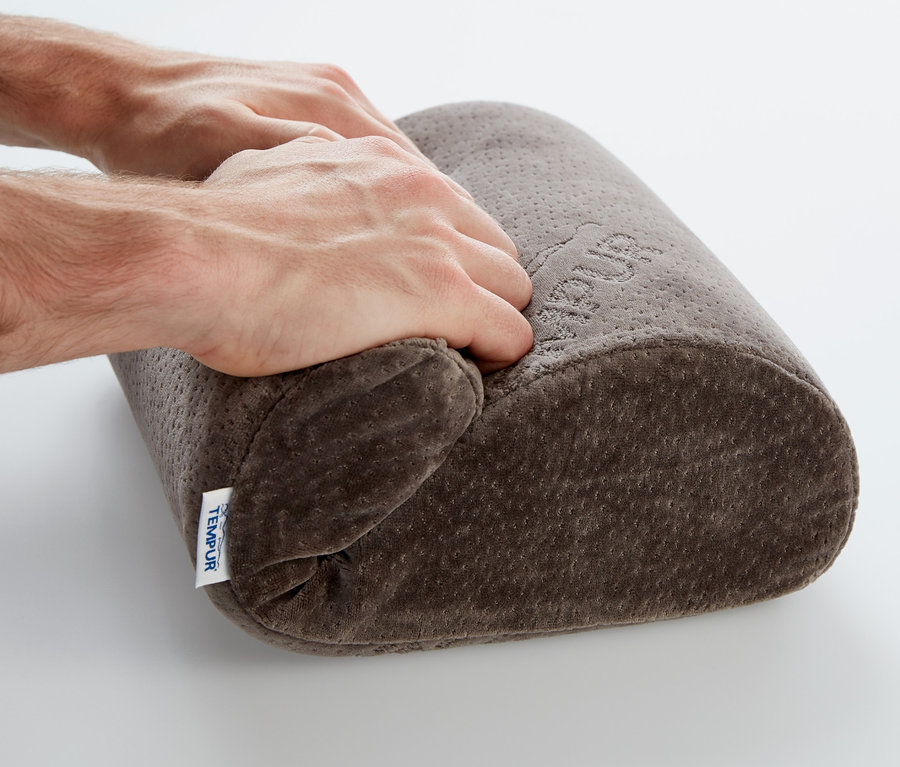 Hände drücken ein braunes TEMPUR® Reisekissen auf einem weißen Hintergrund.