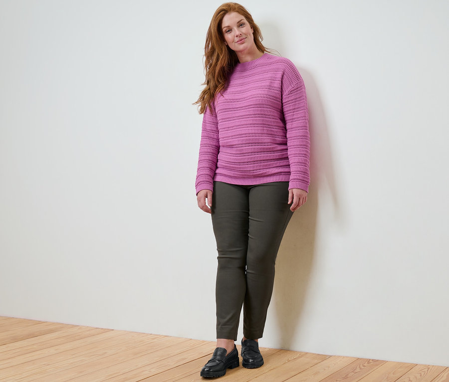 Frau posiert in Pullover mit Ajour-Muster und Stretchhose.