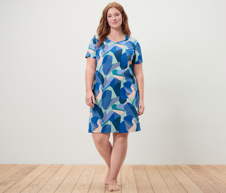 Frau steht barfuß und trägt ein blau gemustertes Nachthemd.