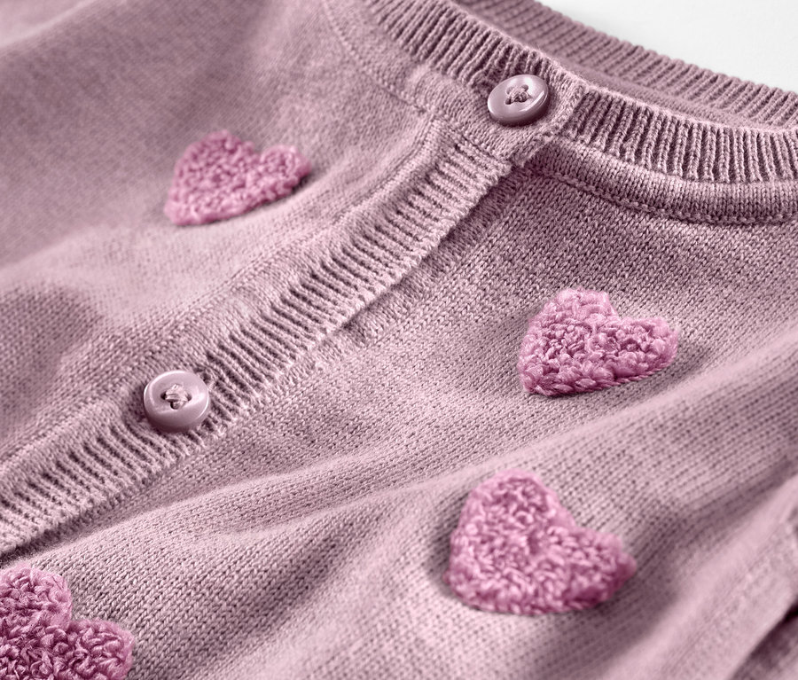 Detailaufnahme einer Kinder-Strickjacke mit aufgenähten rosa Herzen und Knöpfen.