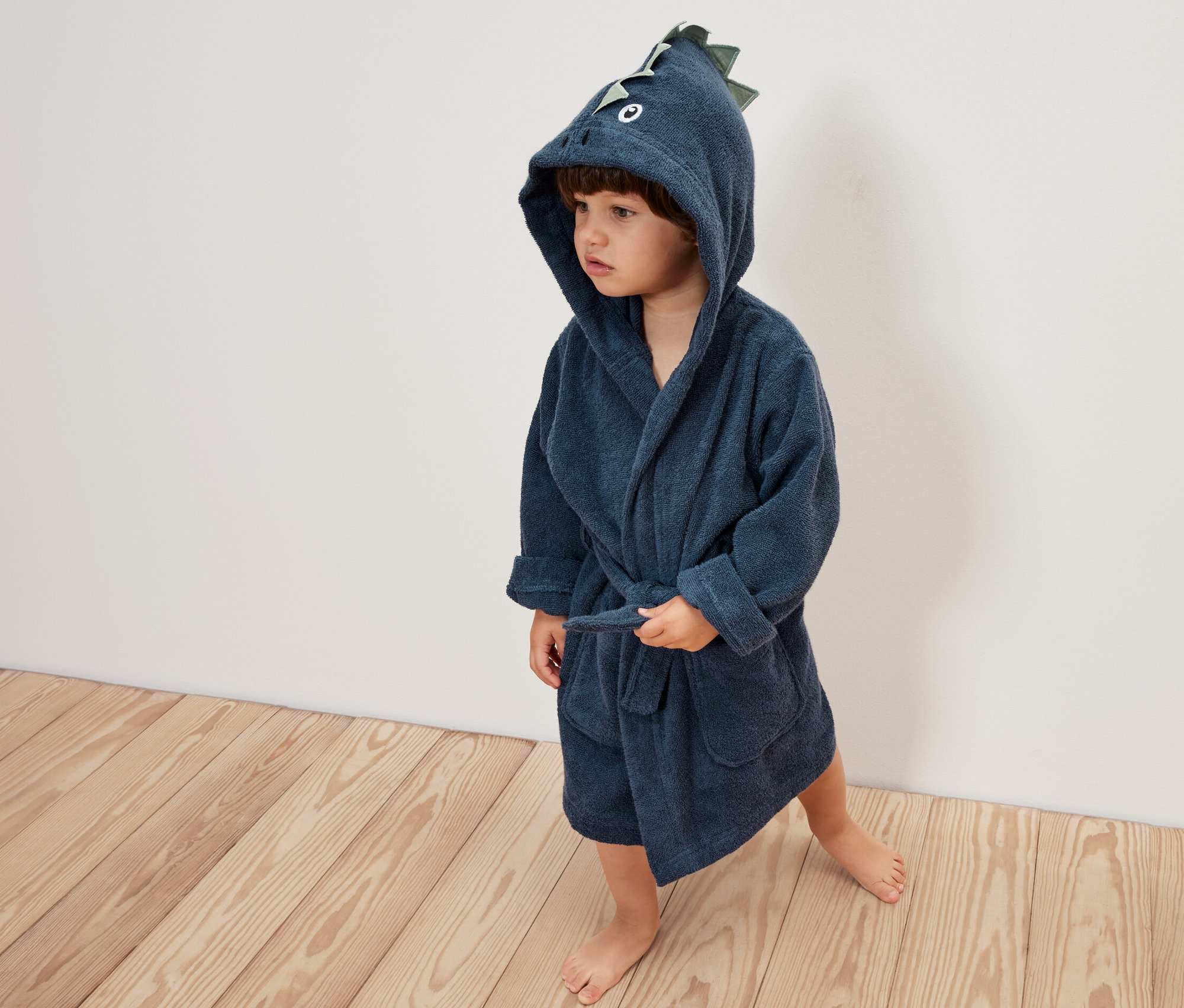 Kleiner Junge trägt einen blauen Kinder-Bademantel mit Drachenmotiv auf der Kapuze.