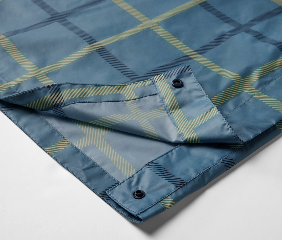 Detailaufnahme eines blau karierten Regenponchos mit Ärmeln und Knöpfen.