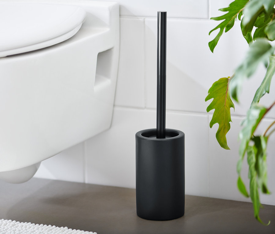Eine schwarze WC-Bürste steht neben einer weißen Toilette.