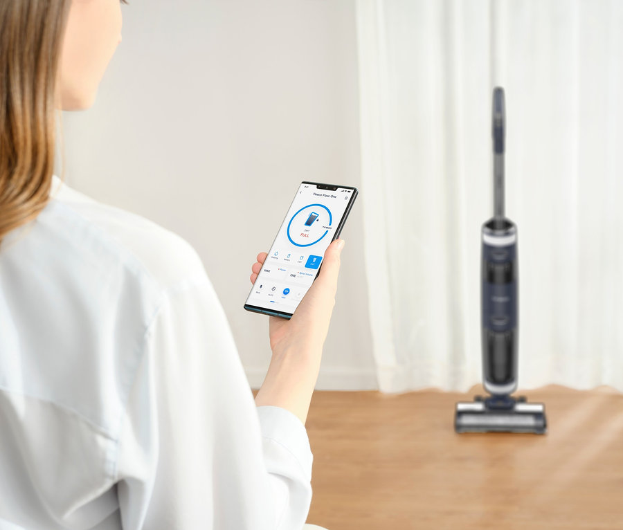 Frau hält ein Smartphone mit App, im Hintergrund ein Tineco Floor One S3 Extreme Nass-Trockensauger.