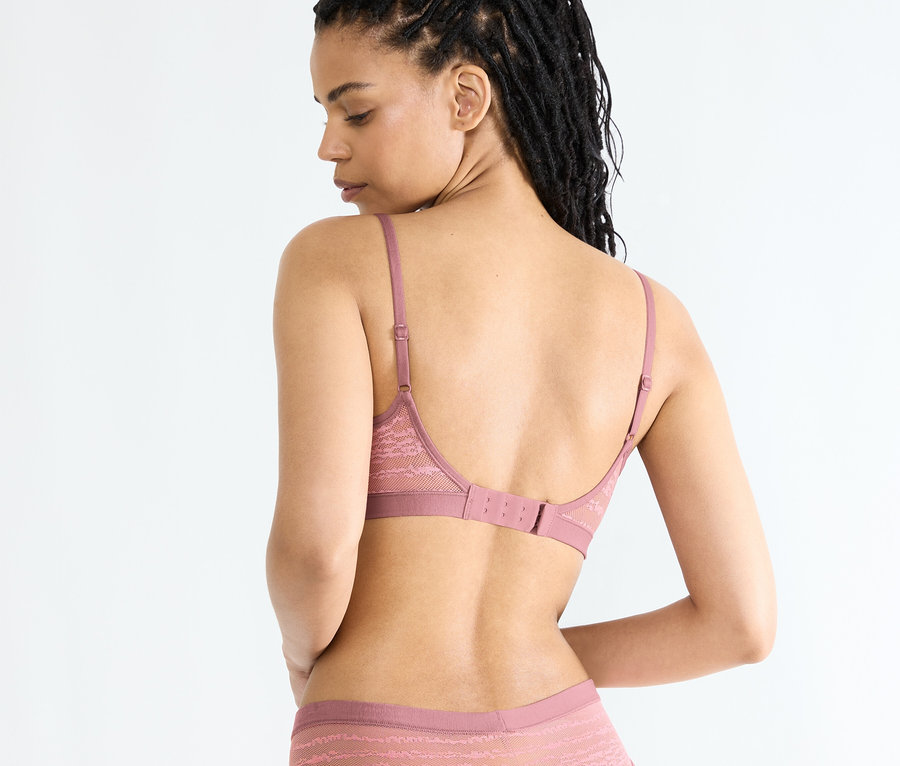 Frau von hinten, trägt einen sloggi FREE Evolve PU Lace BH in Date Night Pink und passende Unterwäsche.