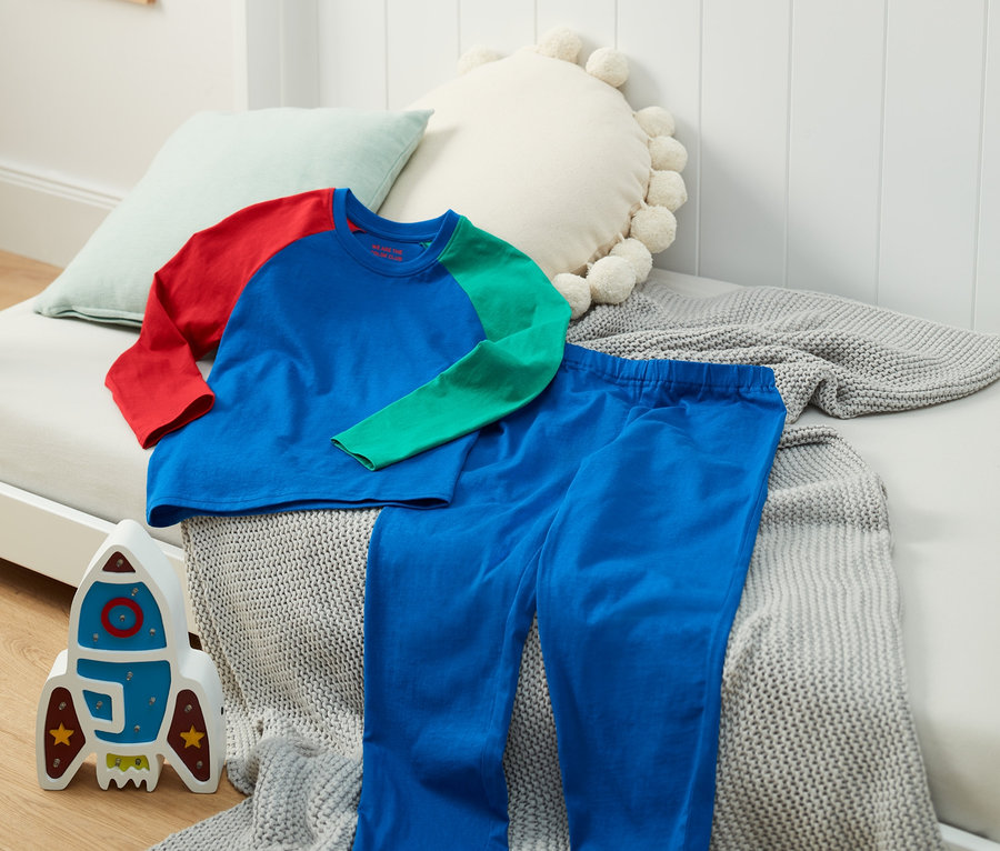Ein Pyjama mit bunten Ärmeln und blauen Hosen liegt auf einem Bett.