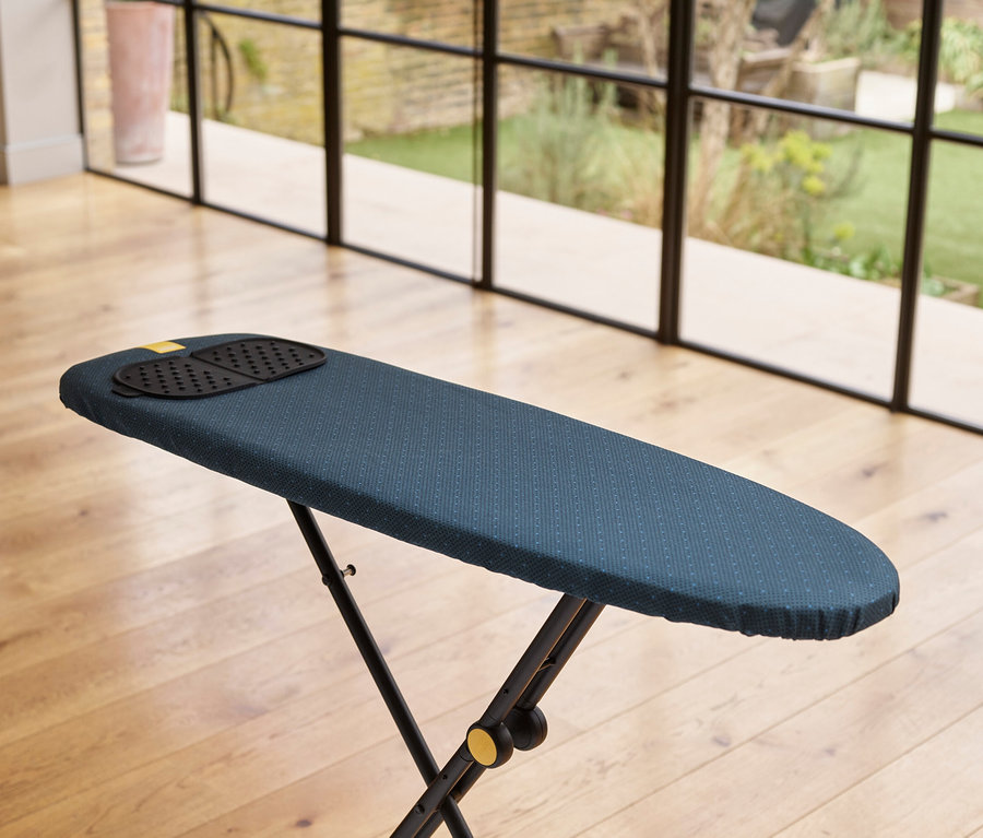 Blaues Bügelbrett mit schwarzer Bügeleisenablage auf Holzboden.