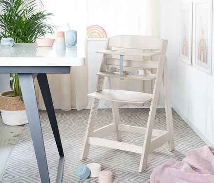 Heller Holz-Kinderhochstuhl roba Sit Up Flex steht auf grauem Teppich neben Tisch.