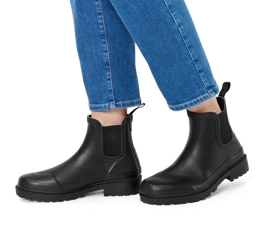 Beine in blauen Jeans und schwarzen Gummistiefeln auf weißem Hintergrund.