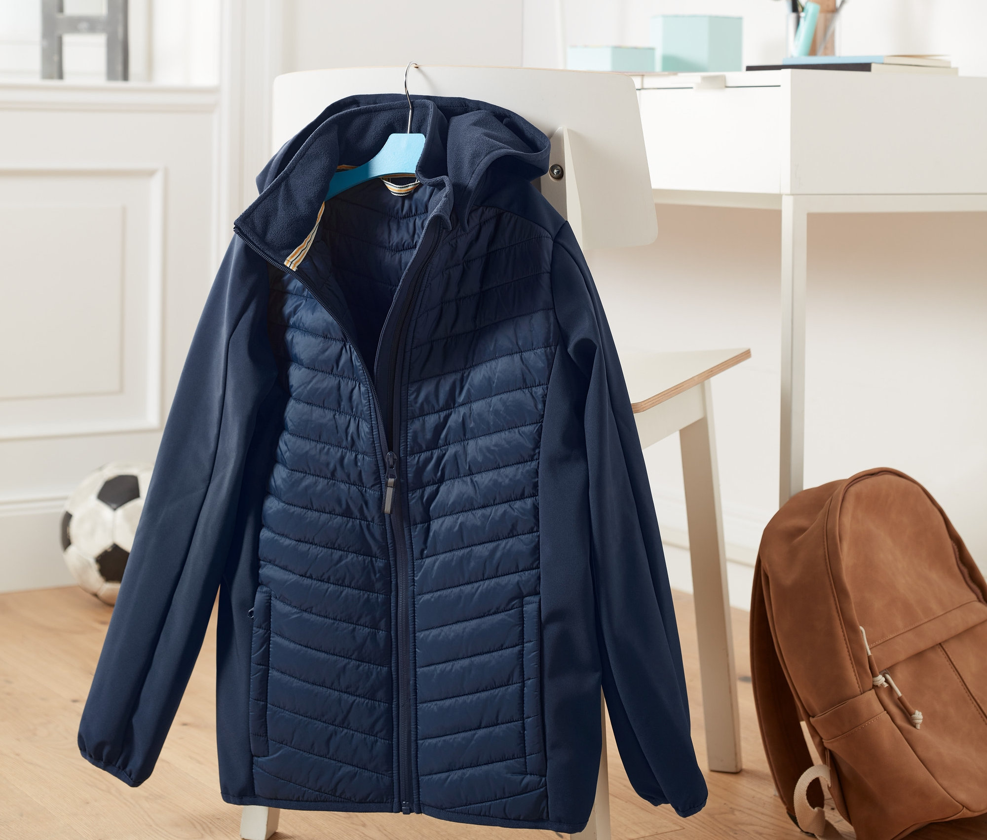 Dunkelblaue Hybrid-Softshelljacke aus recyceltem Material hängt an einem Stuhl.