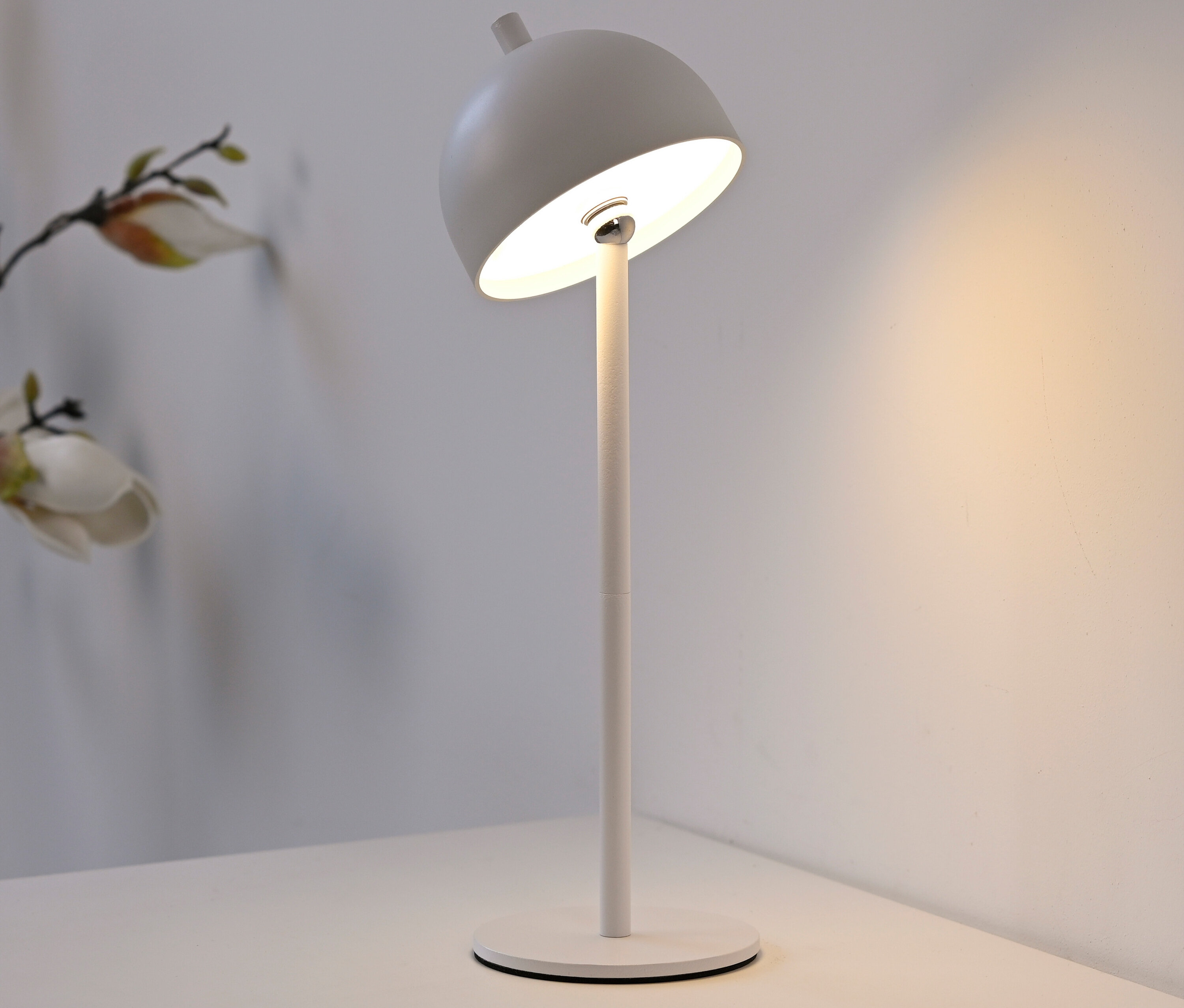 Eine weiße Lampe steht auf einem weißen Nachttisch neben einer Vase mit Blumen.