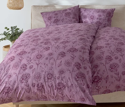 Schlafzimmer mit einem Bett mit lila Blumendruck-Bettwäsche und zwei Kissen.