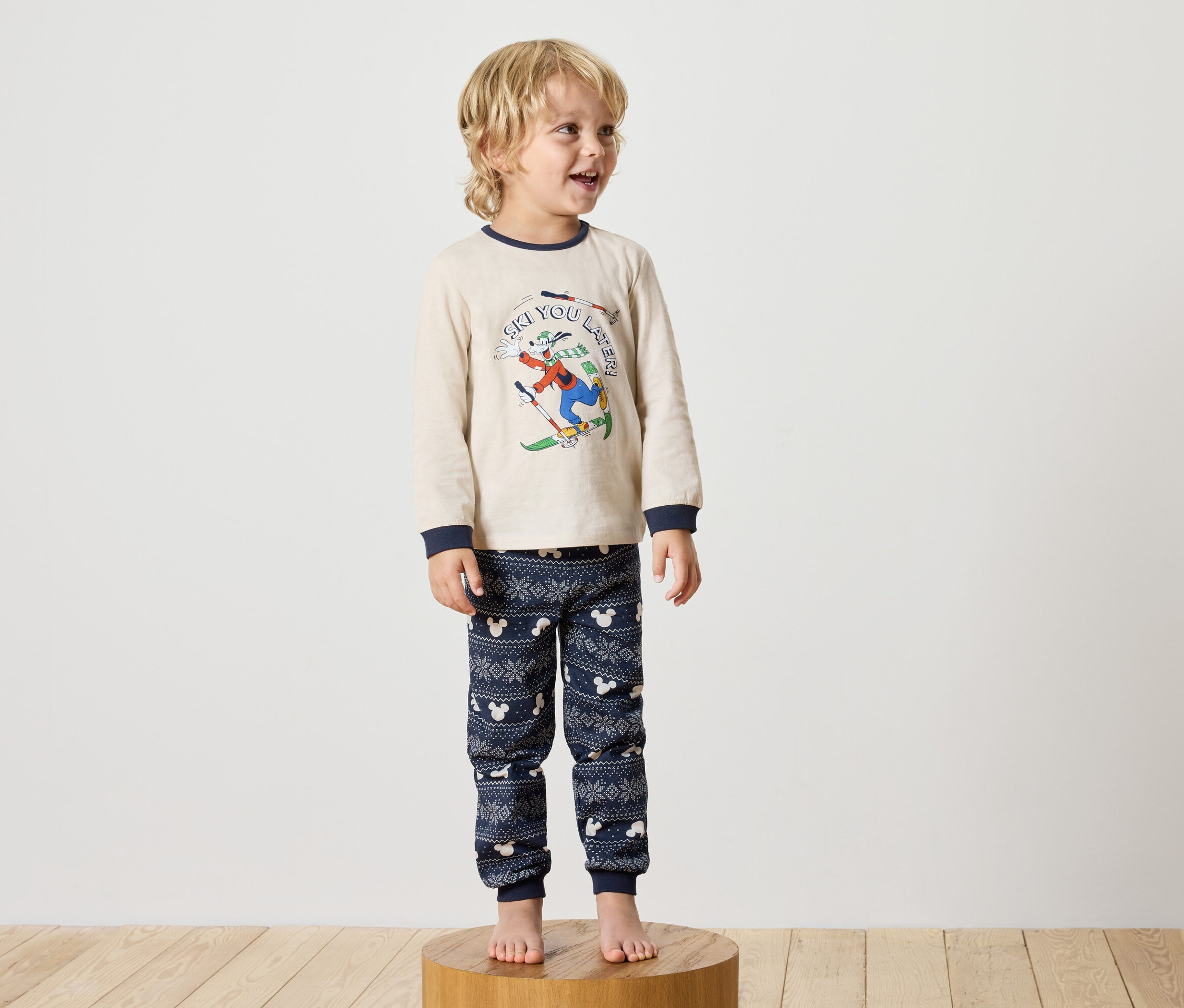 Ein Junge steht auf einem Holzsockel und trägt einen Disney-Pyjama.