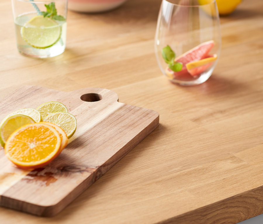 Orangen- und Limettenscheiben auf einem Holzbrett neben einem Getränkeglas und einer Obstschale.