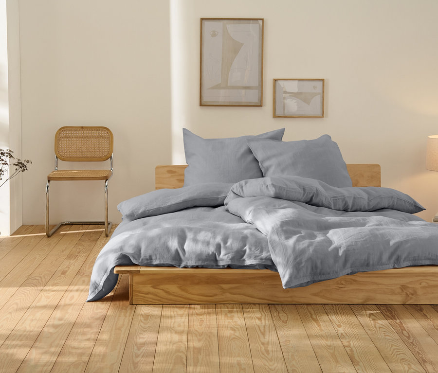 Graue Leinen-Bettwäsche in Übergröße auf einem Holzbett.