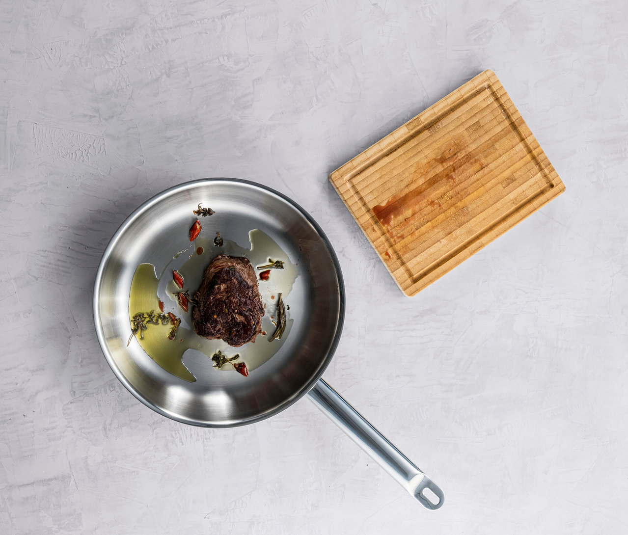 Braten in einer ZWILLING PRO Edelstahlpfanne, daneben ein Schneidebrett.