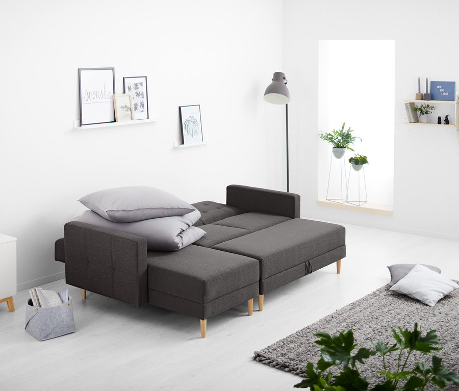 Im Wohnzimmer steht ein Federkern-Eckschlafsofa mit Stauraumbank, auf dem Kissen und eine Decke liegen.