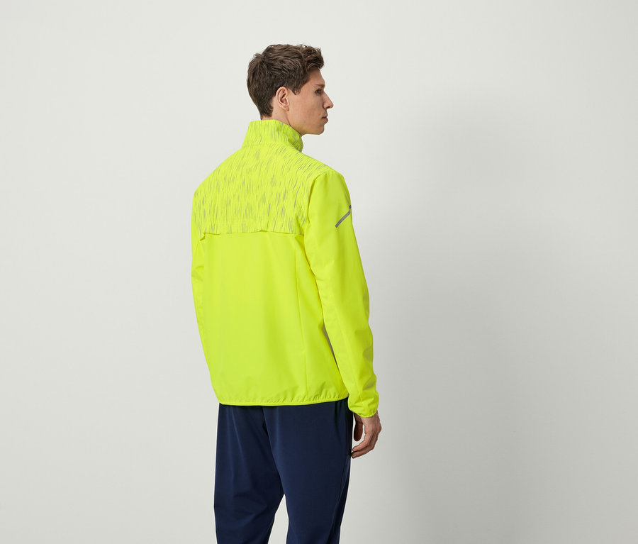 Mann in neongelber Laufjacke und marineblauer Hose, der mit dem Rücken zur Kamera steht.