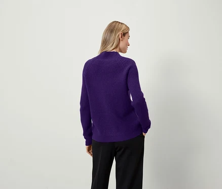 Frau mit dem Rücken zur Kamera trägt einen lila Pullover und eine schwarze Hose.