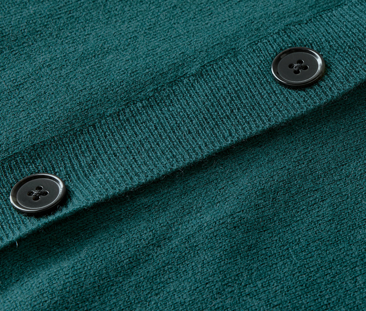 Detailaufnahme eines grünen Strickcardigans mit Knöpfen.