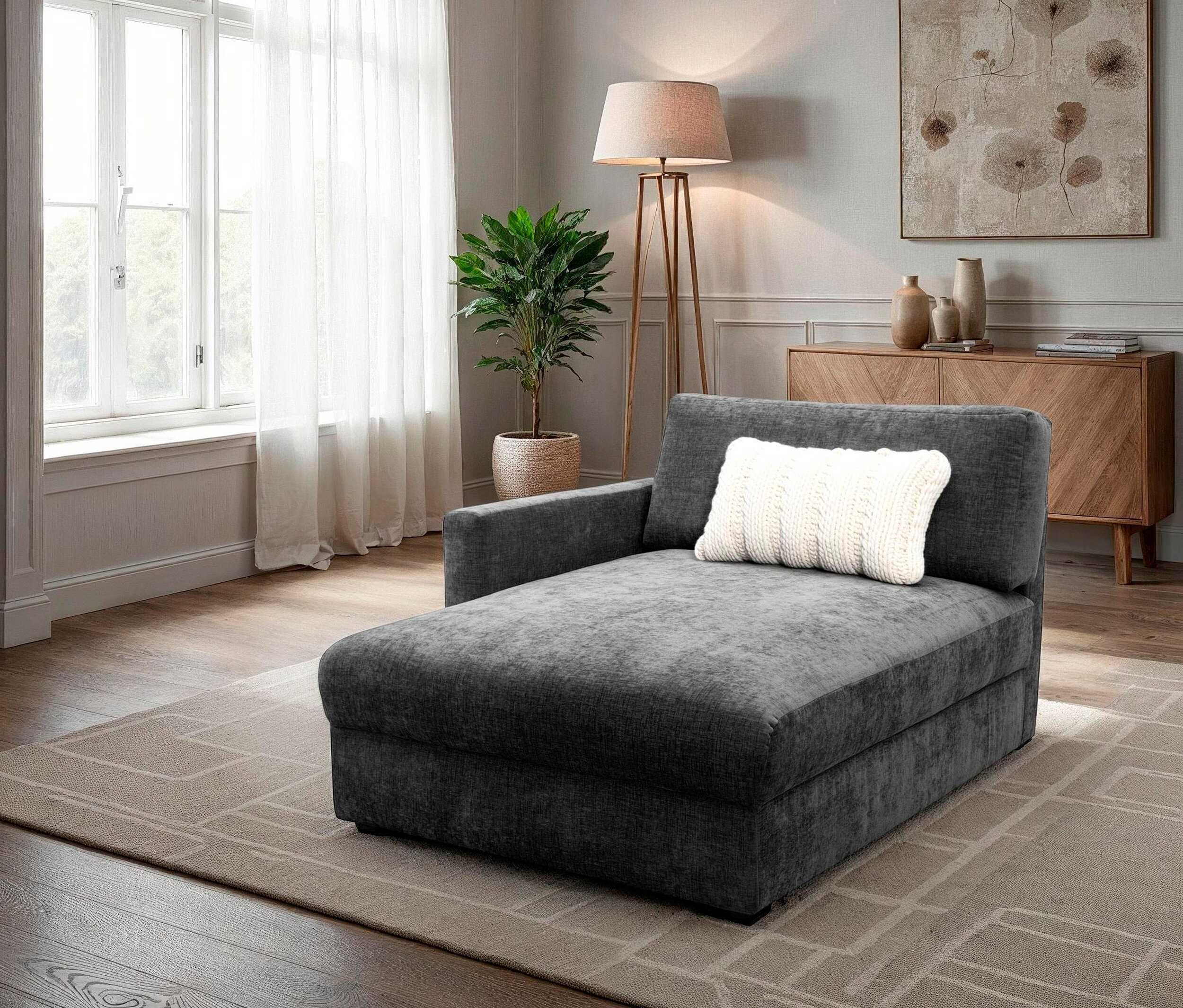 Graue Chaiselongue mit weißem Kissen auf beigem Teppich in einem Wohnzimmer.