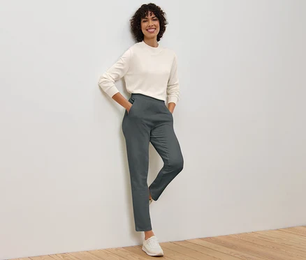 Eine Frau posiert an einer Wand, sie trägt eine graue Joggpants und einen Pullover.