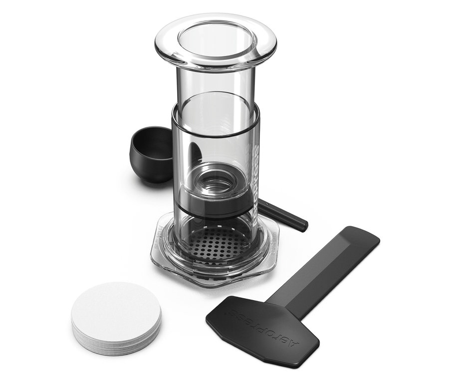Nahaufnahme eines Aeropress Kaffeebereiters mit Zubehör wie einem Messlöffel, einem Rührstab, einem Schaber und Papierfiltern.