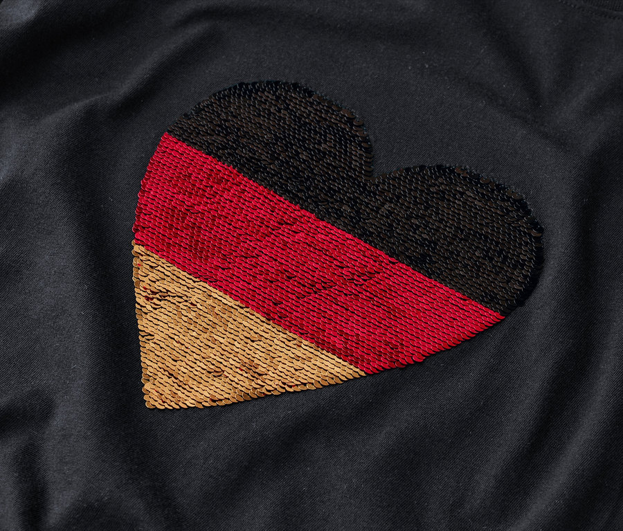Auf einem dunklen Stoff ist ein Herz in den Farben der deutschen Flagge abgebildet.