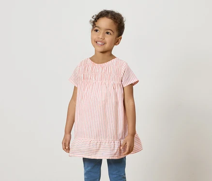 Ein lächelndes junges Mädchen trägt ein rosa-weiß gestreiftes Hemd und blaue Jeans.