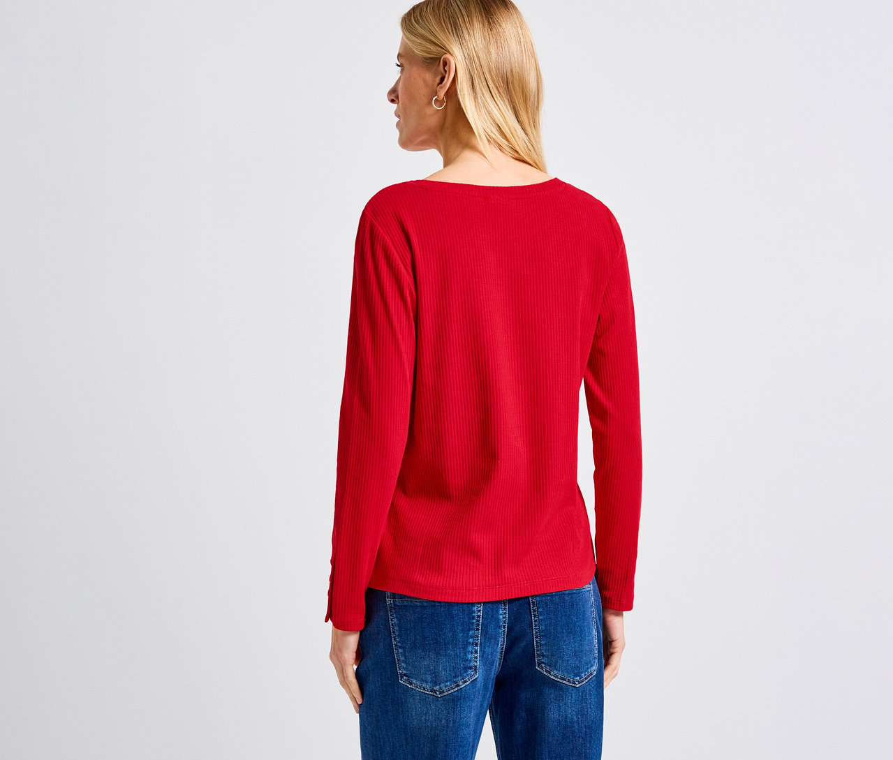 Eine blonde Frau von hinten trägt ein rotes Street One Rippshirt und Jeans.