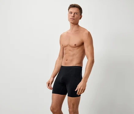 Ein Mann mit freiem Oberkörper steht in schwarzen Boxershorts vor einem weißen Hintergrund.