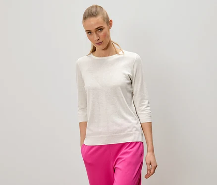 Frau mit blonden Haaren trägt einen hellen Pullover und pinke Hosen.
