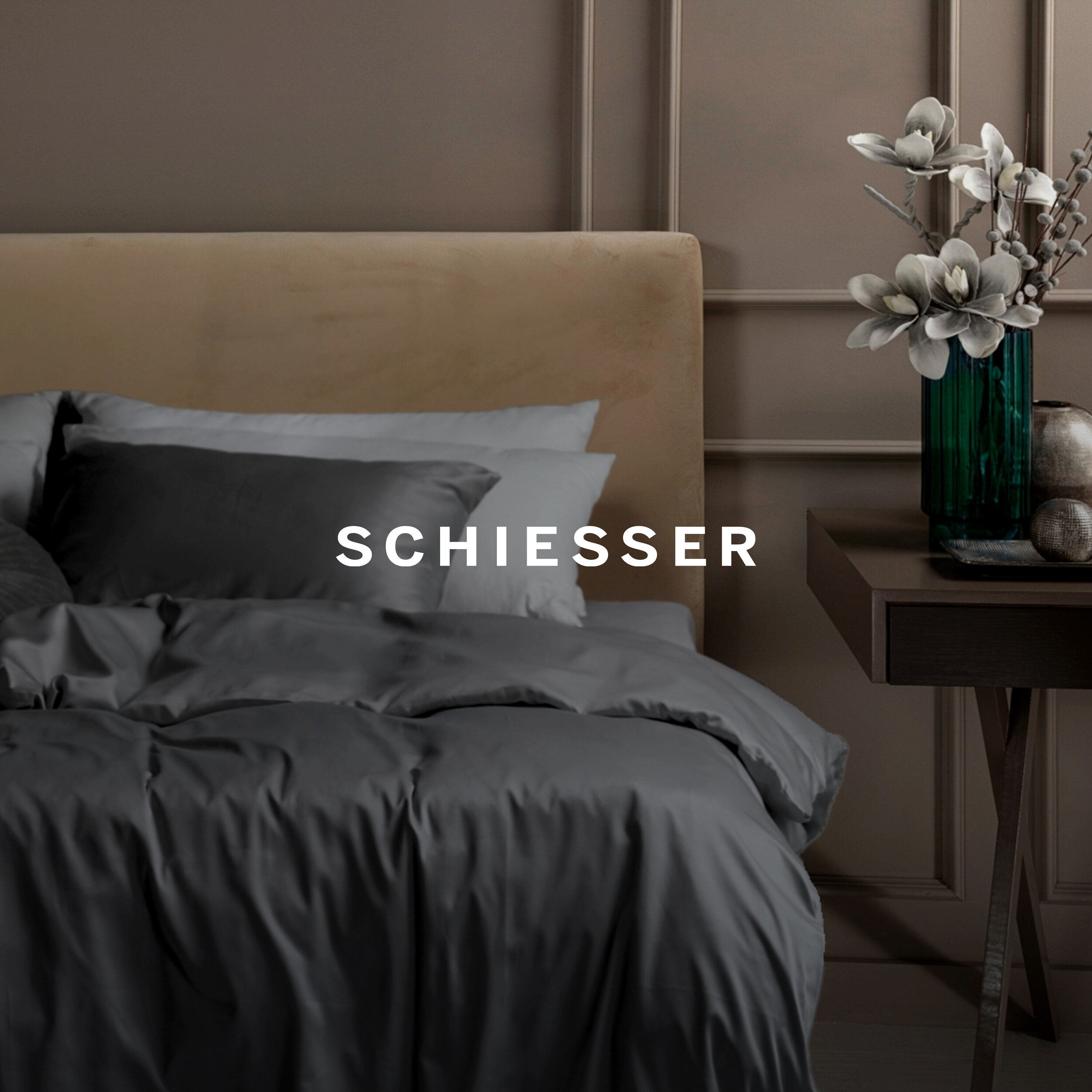 Graue Bettwäsche auf einem Bett mit beigem Kopfteil, neben einem Holztisch mit Blumenvase.